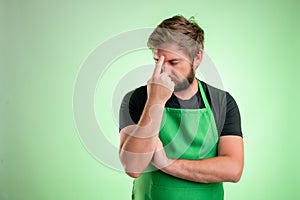 Supermarket employee with green apron and black t-shirt wondering