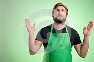 Supermarket employee with greenapron and black t-shirt with open arms looking up