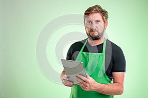 Supermarket employee with greenapron and black t-shirt takes notes