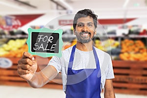 Supermarket employee presenting board with for sale text