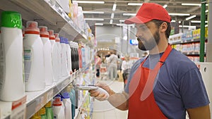 Supermarket employee in red uniform scanning cleaners barcode in modern retail store
