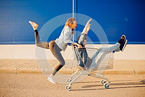 Supermarket, happy young woman carrying man in cart store for shopping, hands raised up. Couple family sunset