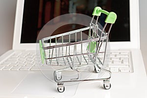 Supermarket shopping cart on laptop background close-up