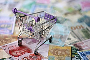 Supermarket trolley on many banknotes of different currency. Background of shopping worldwide