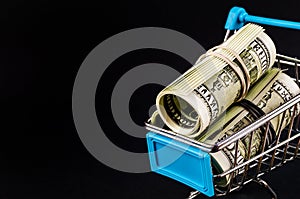 Supermarket trolley with money inside on dark background