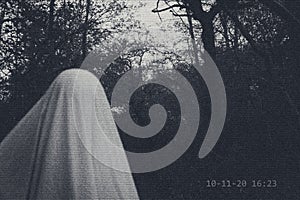 A supernatural concept. Of a ghost with sheet over it`s head. caught on surveillance camera. In a spooky, winter forest