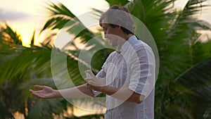 Superslowmotion shot of a young man applying an antimosquito repellent spray on his skin. A tropical background