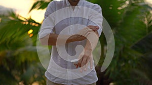Superslowmotion shot of a young man applying an antimosquito repellent spray on his skin. A tropical background