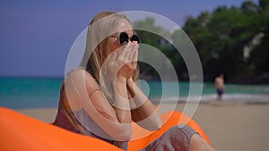 Superslowmotion shot of a young woman coughing while sitting on an inflatable sofa on a tropical beach. travel sickness