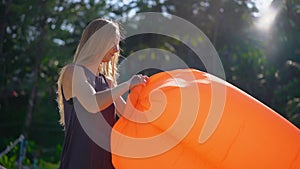 Superslowmotion shot of a young woman on a tropical beach inflating an inflatable sofa. Summer vacation concept