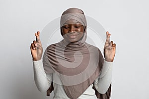 Superstitious Black Muslim Woman In Hijab Making Wish With Crossed Fingers