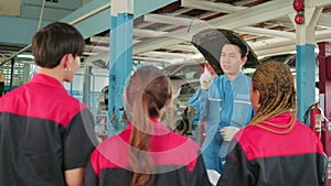 Supervisor engineer is teaching mechanic workers about car engines at a garage.