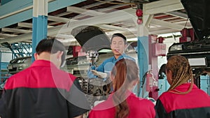 Supervisor engineer is teaching mechanic workers about car engines at a garage.