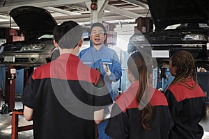 Supervisor engineer is teaching mechanic workers about car engines at a garage.