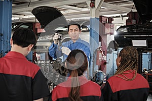 Supervisor engineer is teaching mechanic workers about car engines at a garage.