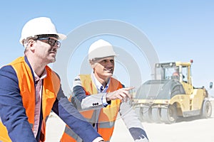 Supervisor explaining plan to colleague at construction site against clear sky