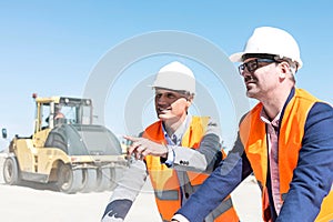 Supervisor explaining plan to colleague at construction site against clear sky