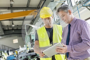 Supervisor and manual worker using digital tablet in metal industry