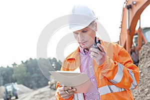 Supervisor reading clipboard while using walkie-talkie at construction site