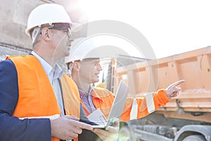 Supervisor showing something to colleague holding laptop at construction site