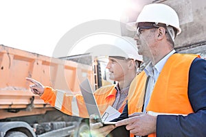 Supervisor showing something to colleague holding laptop at construction site