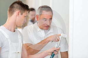 Supervisor talking to apprentice using paint roller