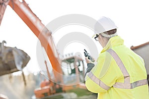 Supervisor using walkie-talkie at construction site against clear sky