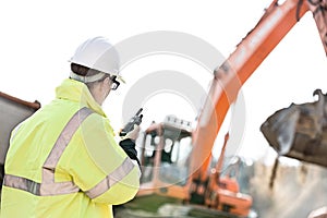 Supervisor using walkie-talkie at construction site against clear sky