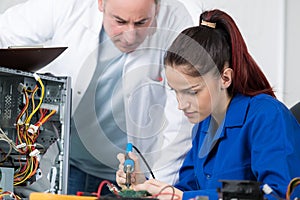 supervisor watching trainee technician solder computer component