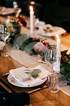 Supper table served for party. Plates, candles, knives, forks on wooden table decorated with branches of greenery. Catering banque