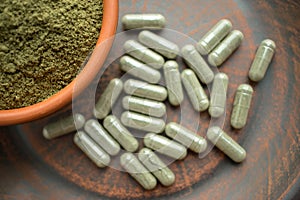 Supplement kratom green capsules and powder on brown plate. Herb