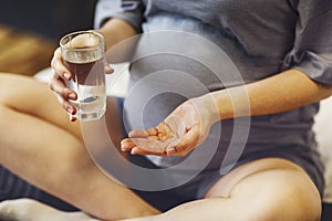 Pregnant woman taking prenatal vitamins during pregnancy, holding water glass and pill in her hands