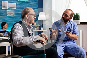 Support assistant worker explaining healthcare treatment to disabled senior man