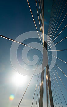 Support and cables of the suspension bridge against the background of the blue sky and the glare of the sunbeam