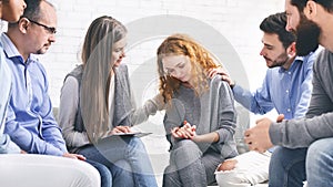 Support group members comforting depressed woman at psychotherapy session