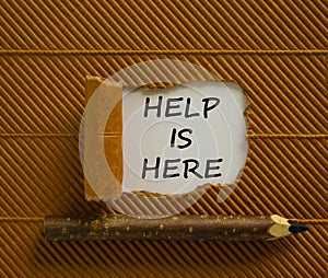 Support and help is here symbol. Words `help is here` appearing behind torn brown paper. Beautiful brown background. Wooden penc