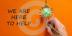 Support symbol. Businessman writing `we are here to help`, isolated on beautiful orange background. Light bulb icon. Business an