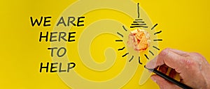Support symbol. Businessman writing `we are here to help`, isolated on beautiful yellow background. Light bulb icon. Business an