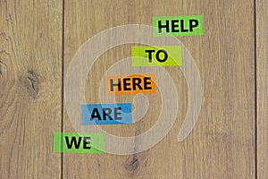 Support symbol. Color papers with words `we are here to help`. Beautiful wooden background, copy space. Business and support