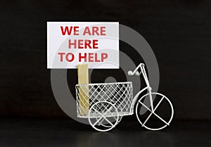 Support symbol. Wooden clothespin with white sheet of paper. Words `we are here to help`. Miniature bicycle model. Beautiful bla