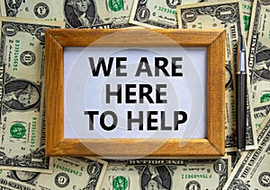 Support symbol. Wooden frame with words `we are here to help` on beautiful background from dollar bills, black pen. Business and