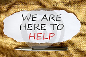 Support symbol. Words `we are here to help` on white paper. Black metallic pen. Beautiful canvas background. Copy space. Busines