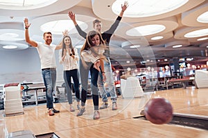 Supporting a girl. Young cheerful friends have fun in bowling club at their weekends