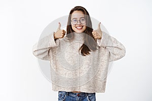 Supportive and optimstic glad nice european female brunette in glasses and sweater showing thumbs up impressed and