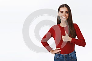 Supportive, upbeat and confident good-looking brunette female in red sweater, showing thumb-up in like or approval, hold