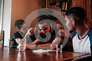 Supportive young men encourage their brokenhearted friend. Arabian guys cheer him up in restaurant. Friendship concept. photo