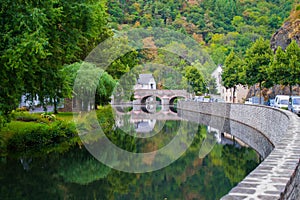 Sure river in Esch-sur-Sure, Luxembourg, with reflections and green vegetation at one side and the stone wall and road in the