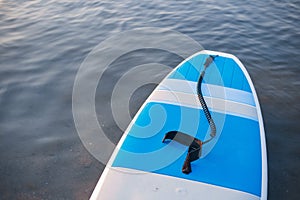 Surf board on blue clean water surface background. SUP boarding equipment in sunset lights close-up. Outdoor water