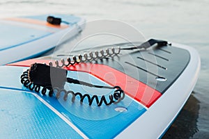 Surf boards on blue clean water surface background. Surfing and SUP boarding equipment in sunset lights close-up