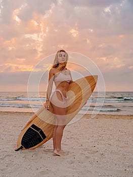 Surf girl in bikini posing with surfboard on beach with sunset or sunrise tones